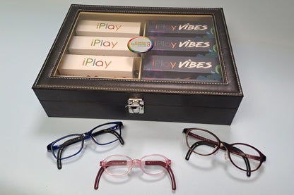 A display box containing four pairs of eyeglasses in different frame colors, with the words 'iPlay' and 'VIBES' visible on the inside packaging. The glasses are arranged in front of the box on a light gray background.